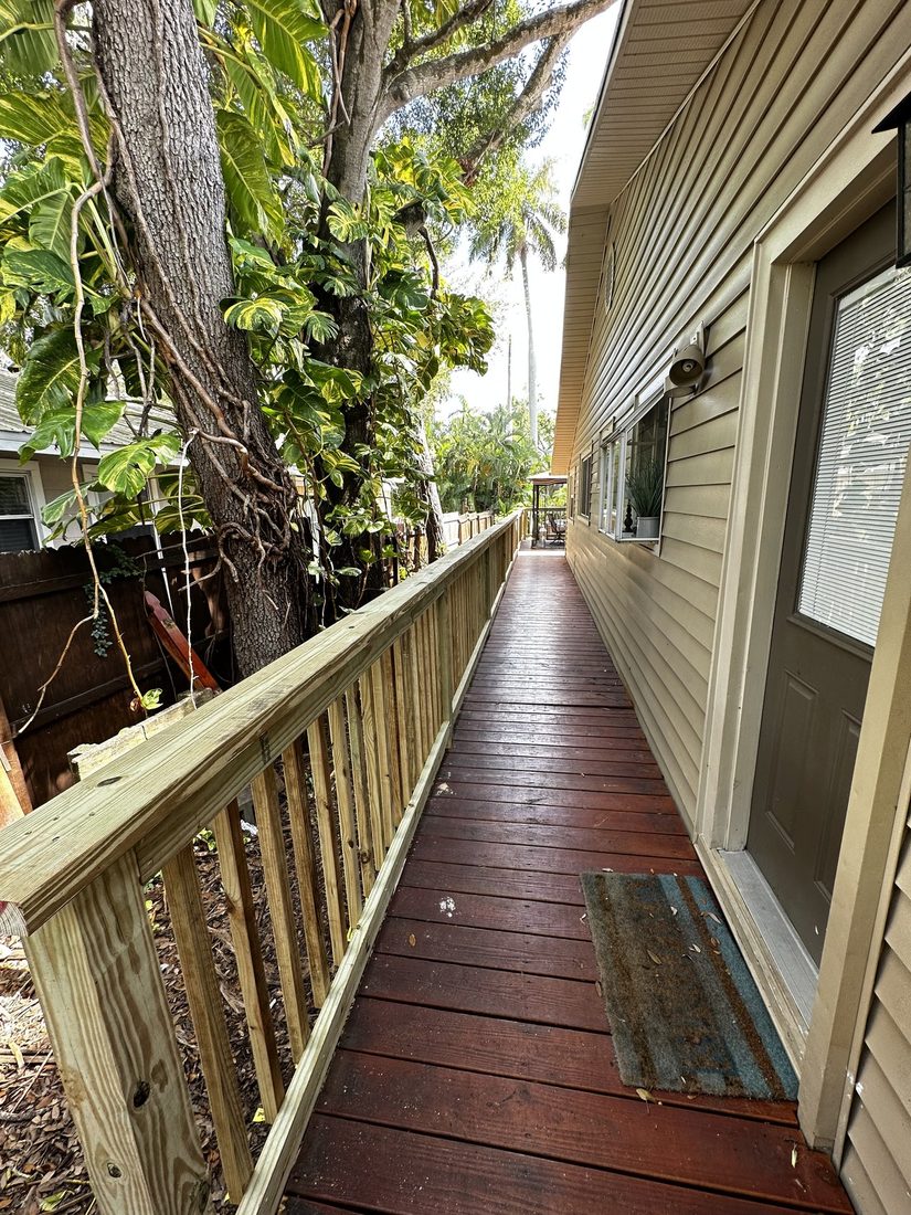 Stained deck walkway with railing beside a home