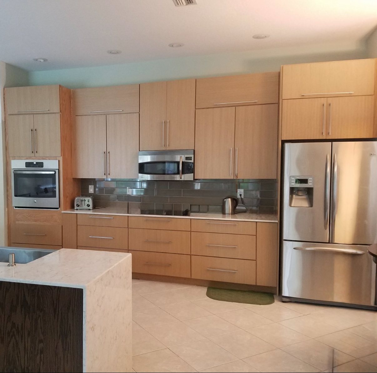 Kitchen with light wood cabinetry, glass tile backsplash, and a quartz island